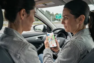 Femme consultant une carte d'autoroute française sur son smartphone depuis l'habitacle d'une voiture garée sur une aire de repos