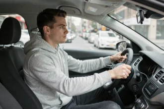 Jeune homme assis au volant d'une voiture en ville, réfléchissant avant de conduire sans permis complet